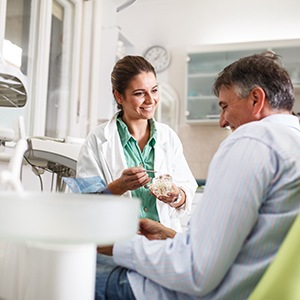 Smiling dentist showing patient model of teeth