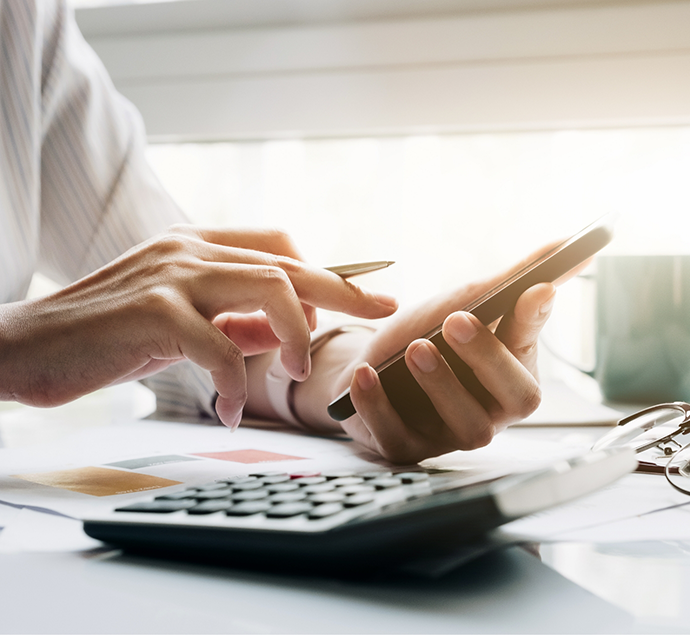 Person typing on their phone at a desk next to a calculator